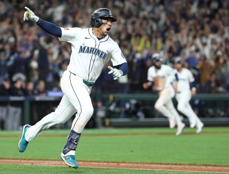 A packed T-Mobile Park stadium at night, illuminated under bright lights, with Seattle Mariners players celebrating on the field after Jorge Polanco’s walk-off single in the 15th inning of ALDS Game 5 against the Detroit Tigers on October 10, 2025. Fans in the stands cheer wildly, waving blue and teal flags, capturing the electric atmosphere of the historic victory.