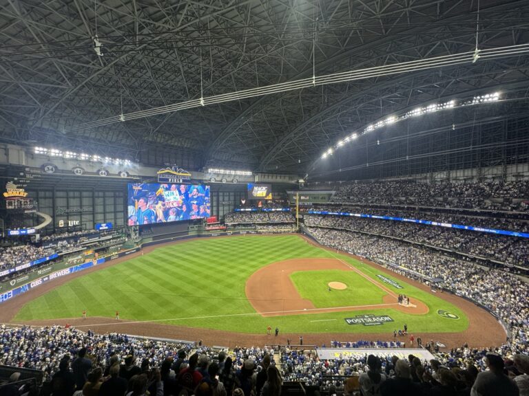 Dynamic action shot of Milwaukee Brewers players celebrating a home run during the 2025 NLDS Game 5 against the Chicago Cubs, with fireworks exploding over American Family Field at night.