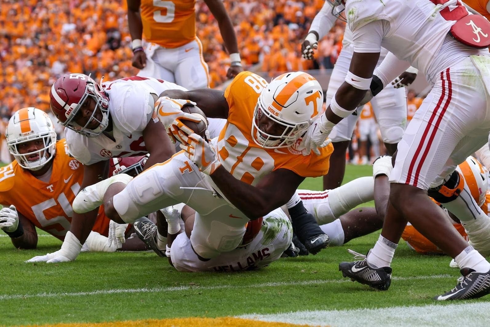 A vibrant stadium scene with Tennessee Volunteers in orange and Alabama Crimson Tide in crimson facing off on the football field, packed with cheering fans, capturing the intensity of the Tennessee vs Alabama rivalry in 2025.