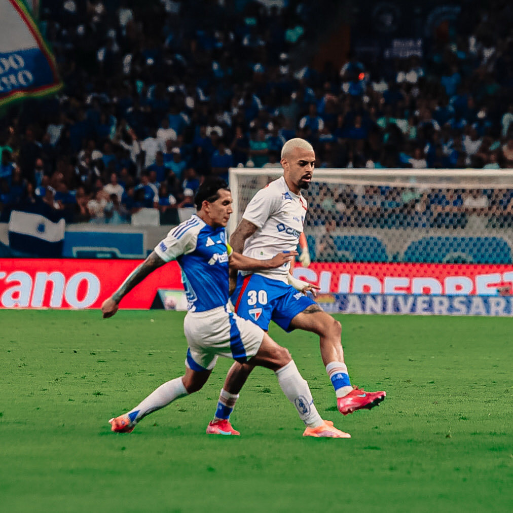 A soccer match scene at Mineirão Stadium, featuring players from Cruzeiro and Fortaleza in action during their Brasileirão 2025 match. The stadium is filled with over 40,000 spectators, with Cruzeiro's blue and white colors prominent. The field shows intense play, with a focus on Christian scoring the decisive goal for Cruzeiro's 1-0 victory.