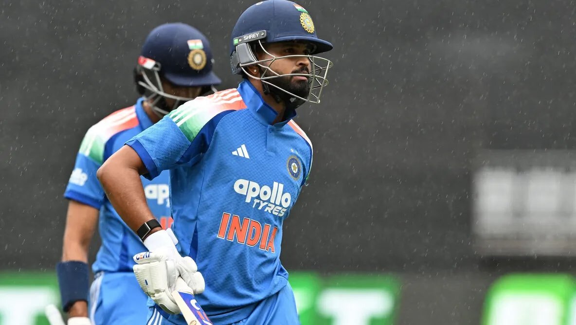 A dynamic action shot of a cricket match between the India national cricket team and the Australian men’s cricket team, featuring an Indian batsman hitting a lofted cover drive against an Australian bowler on a packed stadium field under bright sunlight, with the scoreboard in the background displaying a close contest.