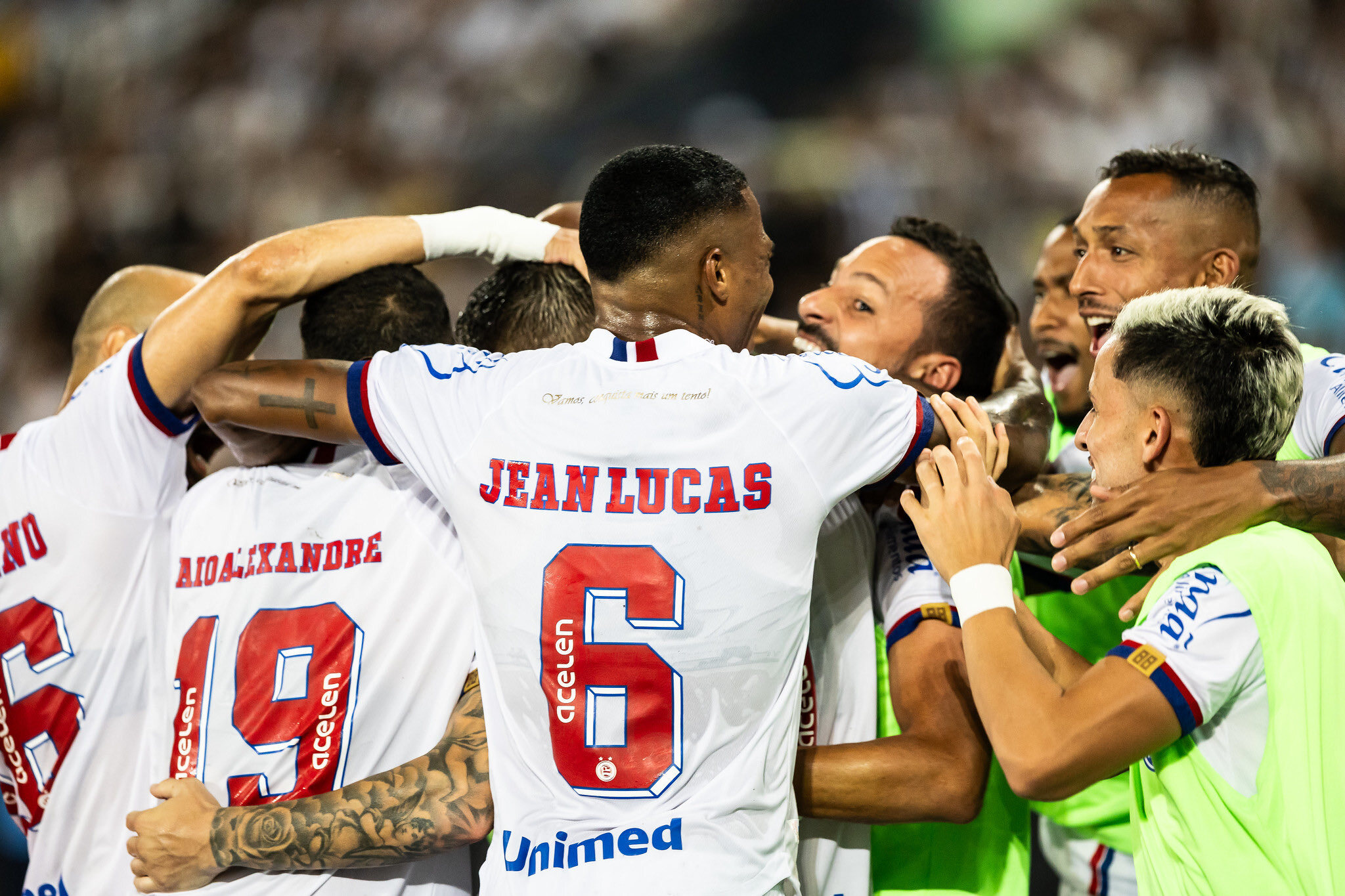 A vibrant football stadium in Salvador, Brazil, filled with passionate EC Vitória and Bahia fans waving red, blue, and white flags during a Ba-Vi derby match, with players on the field and the stands illuminated under bright stadium lights.